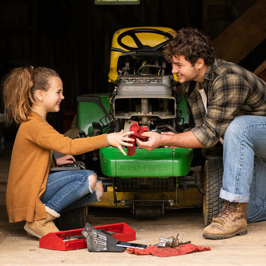 A man and young girl repair a John Deere lawnmower