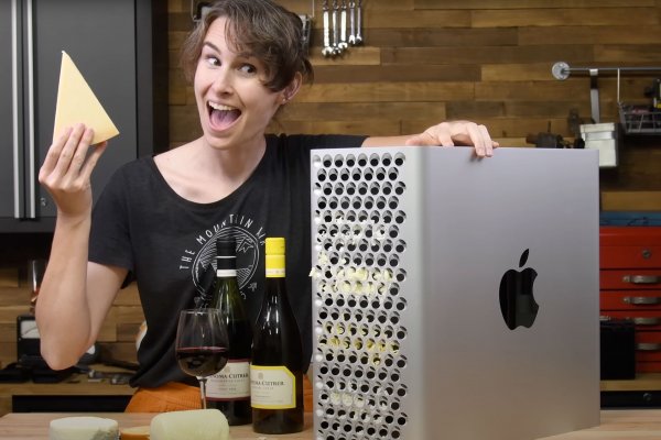 A woman holds a block of cheese up in front of a 2023 Mac Pro case, which is full of cheese.